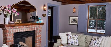 Una sala de estar acogedora con chimenea, un sofá con cojines florales y una ventana con vista a árboles.