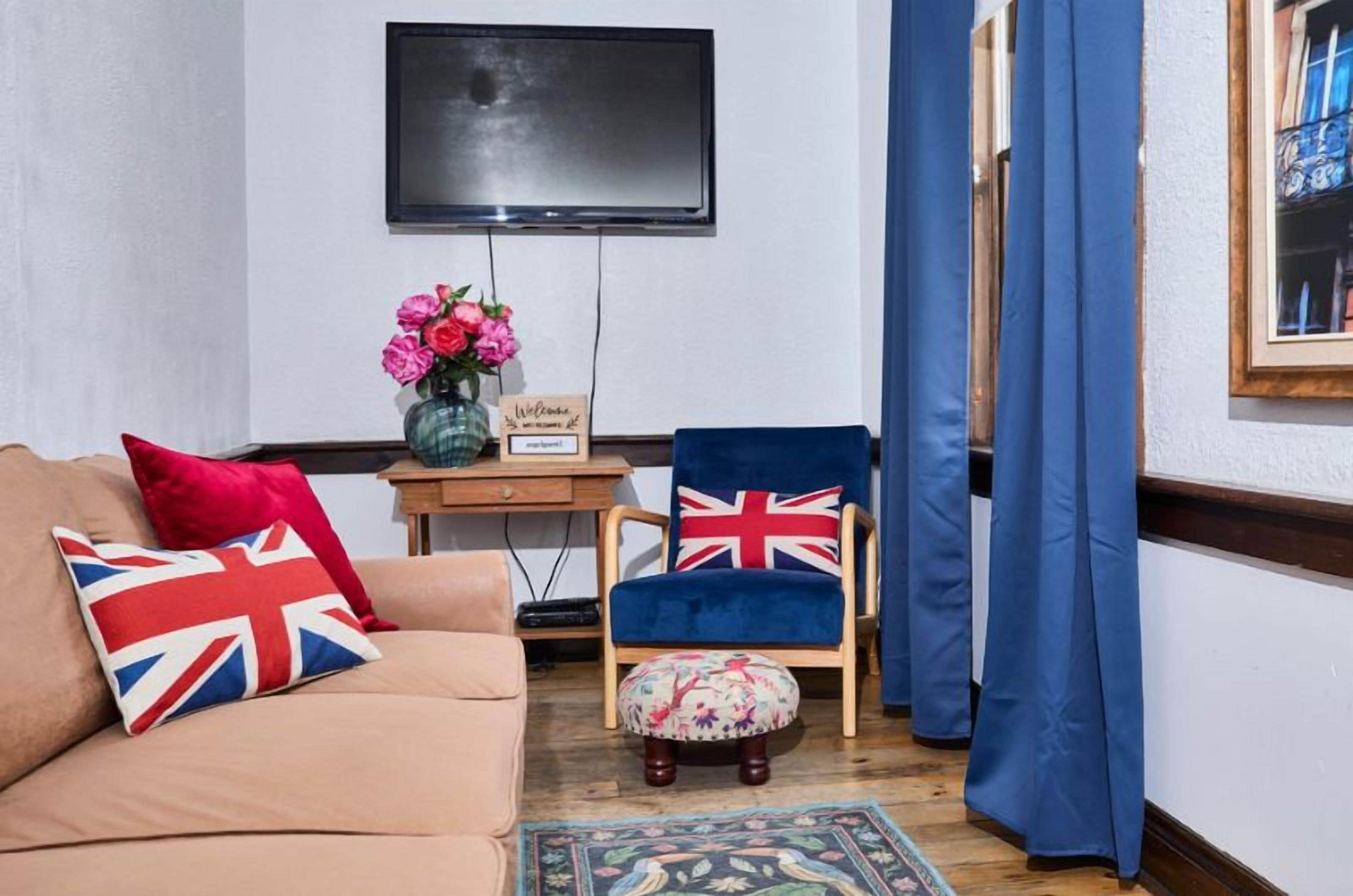 A living room with a sofa, a chair, a small table with a vase of flowers, and a flat-screen TV mounted on the wall.