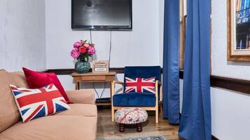 A living room with a sofa, a chair, a small table with a vase of flowers, and a flat-screen TV mounted on the wall.