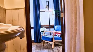 A room with a wooden floor, a blue chair with a Union Jack pillow, and a window with blue curtains.