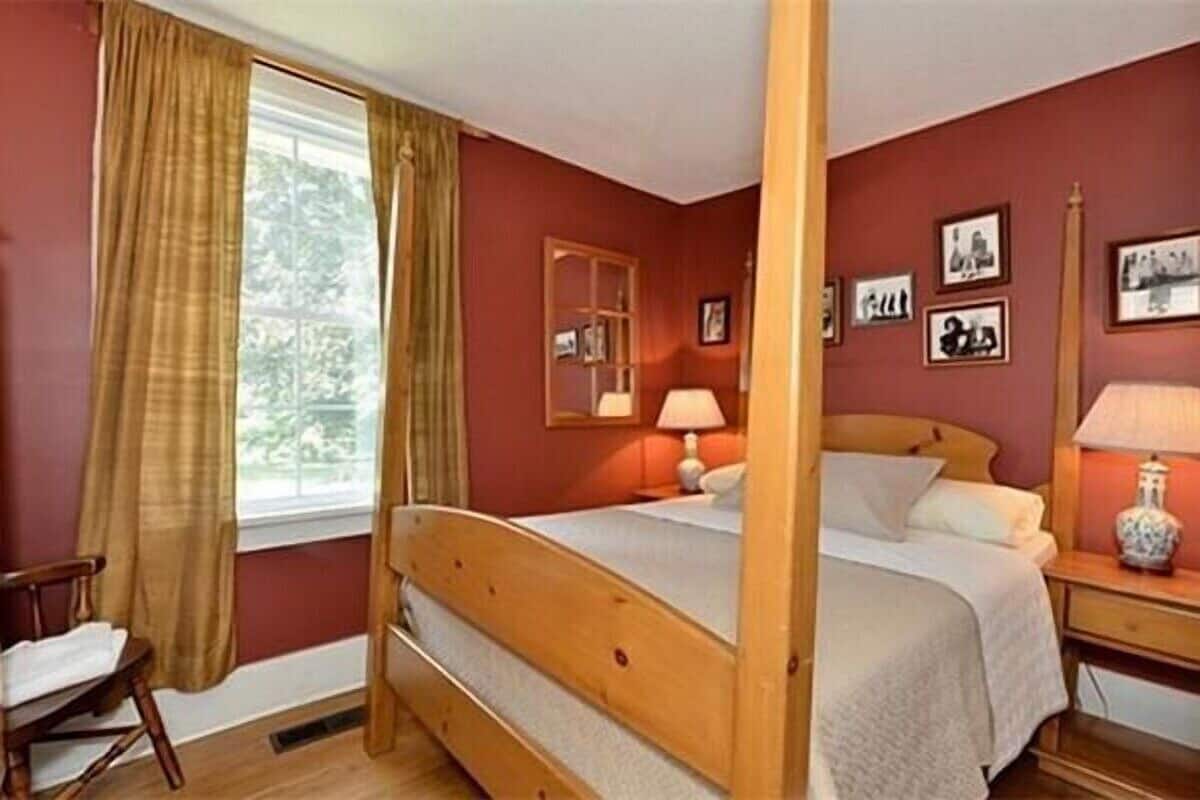 A bedroom with a wooden bed, a window with curtains, a bedside table with a lamp, and framed pictures on the wall.