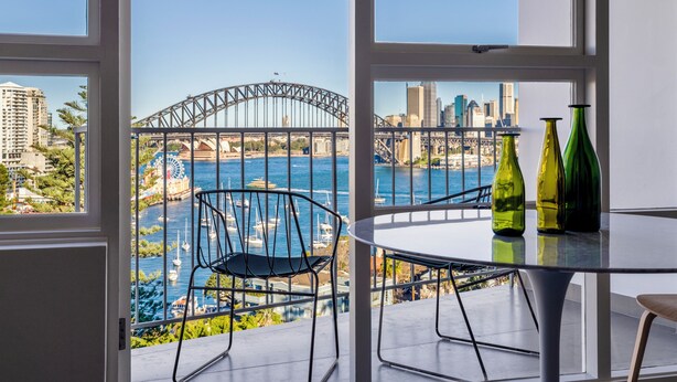 Un balcón con vistas al Puente de Sydney y la Casa de la Ópera de Sydney, que incluye una mesa redonda y dos sillas.