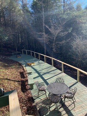 A wooden deck with metal chairs and a table, surrounded by a wooden railing, overlooking a forested area.