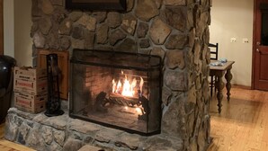 A stone fireplace with a framed picture above it, a fire burning inside, and a wooden ceiling.