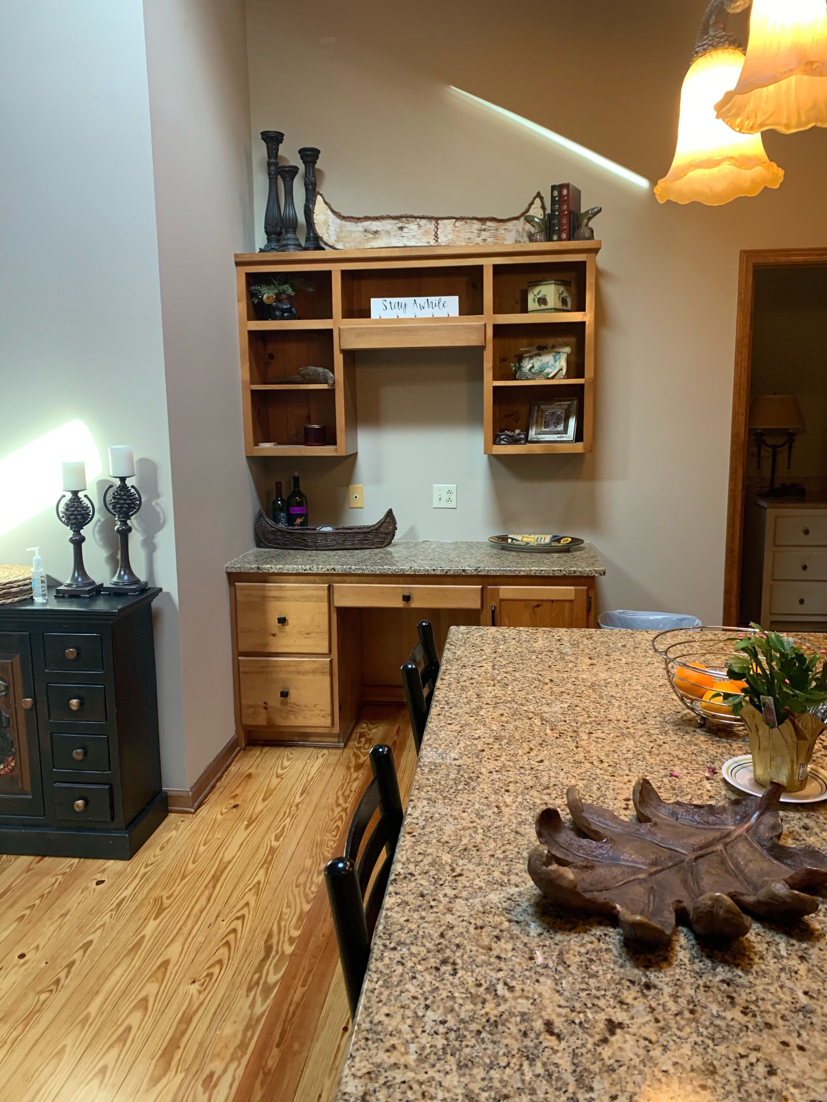 A kitchen with wooden cabinets, a granite countertop, and a sign that reads "Stay Awhile".