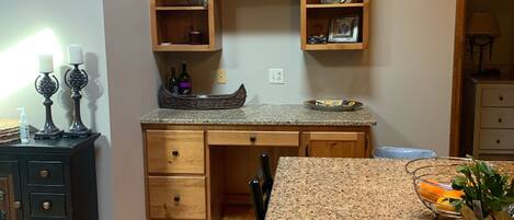 A kitchen with wooden cabinets, a granite countertop, and a sign that reads "Stay Awhile".