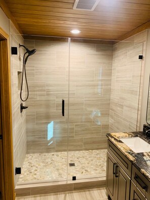 A modern bathroom with a glass-enclosed shower, a marble countertop, and a wooden ceiling.