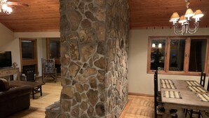 A cozy living room with a stone fireplace, wooden ceiling, and a dining area with a checkered tablecloth.