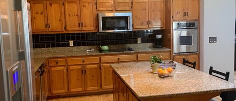 A kitchen with wooden cabinets, a granite countertop, stainless steel appliances, and a hanging light fixture.