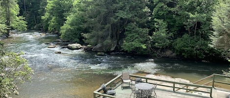 A wooden deck with outdoor seating overlooking a river, surrounded by dense forest.