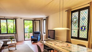 A spacious living room with a large dining table, comfortable seating, a television, and a view of greenery through the windows. - Fiorita by Interhome (Brusino Arsizio)