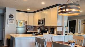 Una cocina moderna con armarios blancos, una isla central y un comedor con sillas de madera.