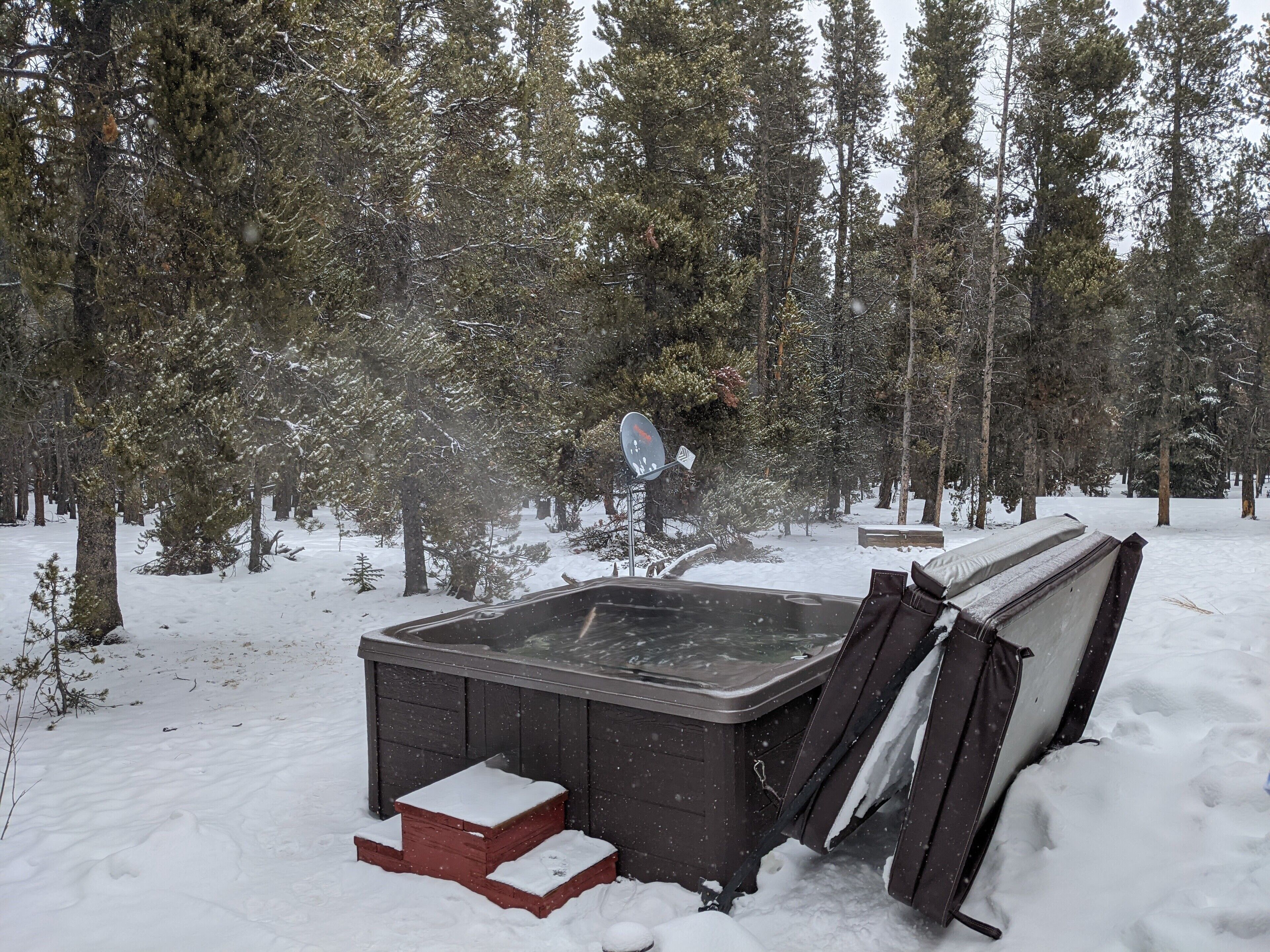 A snow-covered outdoor hot tub in a forested area.