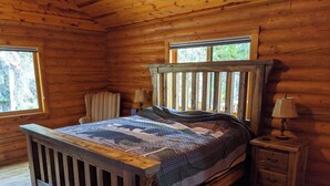 Een slaapkamer in een houten hutje, met een bed, twee nachtkastjes en een raam.