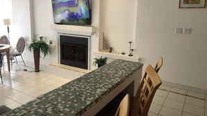 A living room with a fireplace, a television mounted above it, and a dining area with a patterned table. - K38 Club Marena Ground Floor With Big Patio Walkout to Fantastic Surfing (Rosarito)