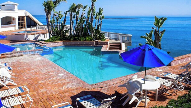 A pool area with clear blue water, surrounded by palm trees and a view of the ocean. - K38 Club Marena Ground Floor With Big Patio Walkout to Fantastic Surfing (Rosarito)