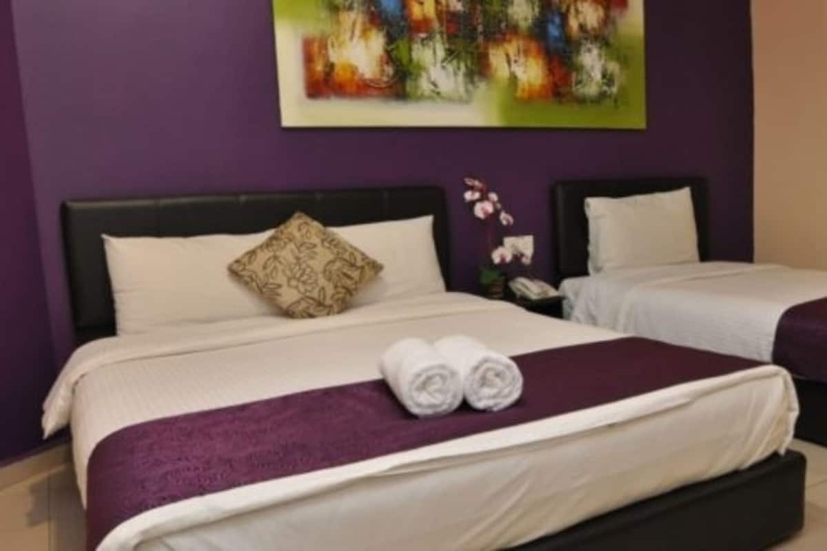 A hotel room with two beds, each with a purple bedspread and white linens, and a large abstract painting on the wall.