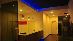 Recepção de hotel com balcão, luminárias pendentes e escada iluminada em azul.