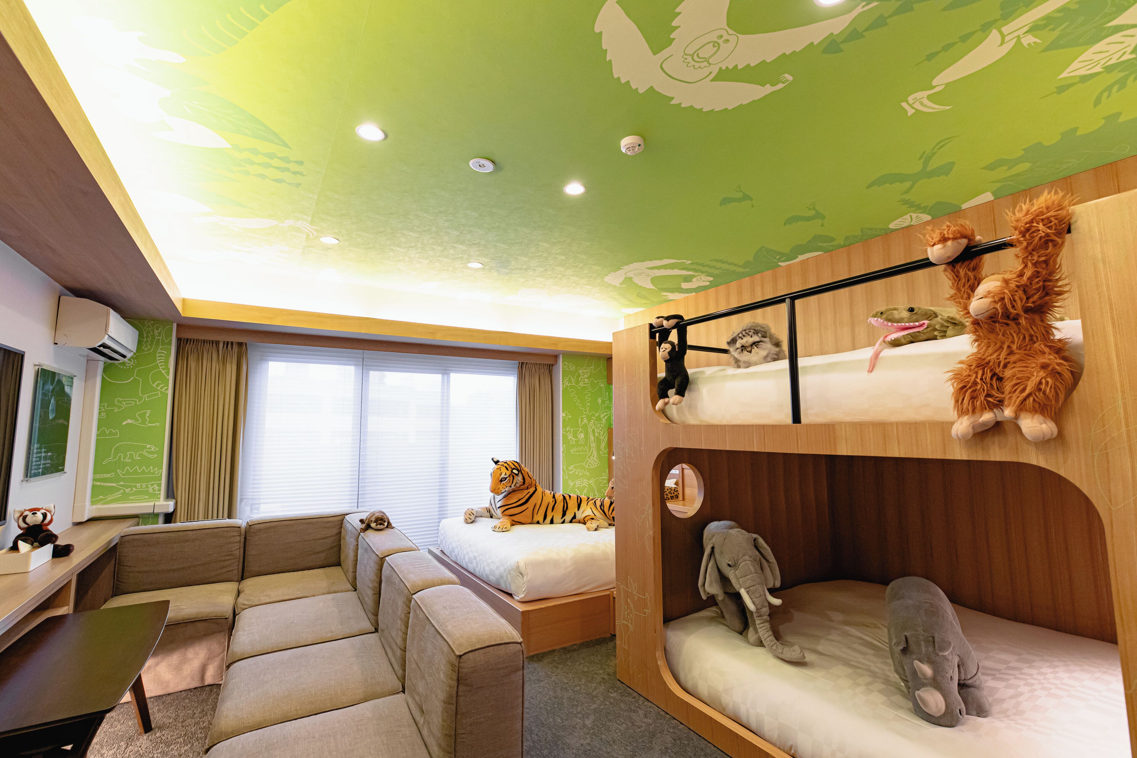 Een kamer met stapelbedden, een slaapbank, een bureau en een tijgerknuffel op het bed.