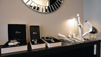 A well-lit hotel reception area with a modern mirror, a black and white checkered wall design, and a counter displaying a jewelry box, a wine glass, and a hairdryer.