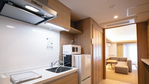 A modern kitchen with a microwave, refrigerator, and sink. There is a dining area with a sofa and a table. - GOLDSTAY SAKAE (Nagoya)