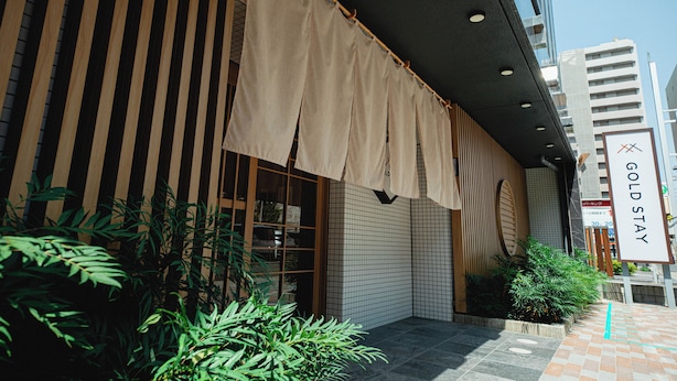A hotel entrance with a beige awning, wooden slats, and a sign reading "GOLD STAY". - GOLDSTAY SAKAE (Nagoya)