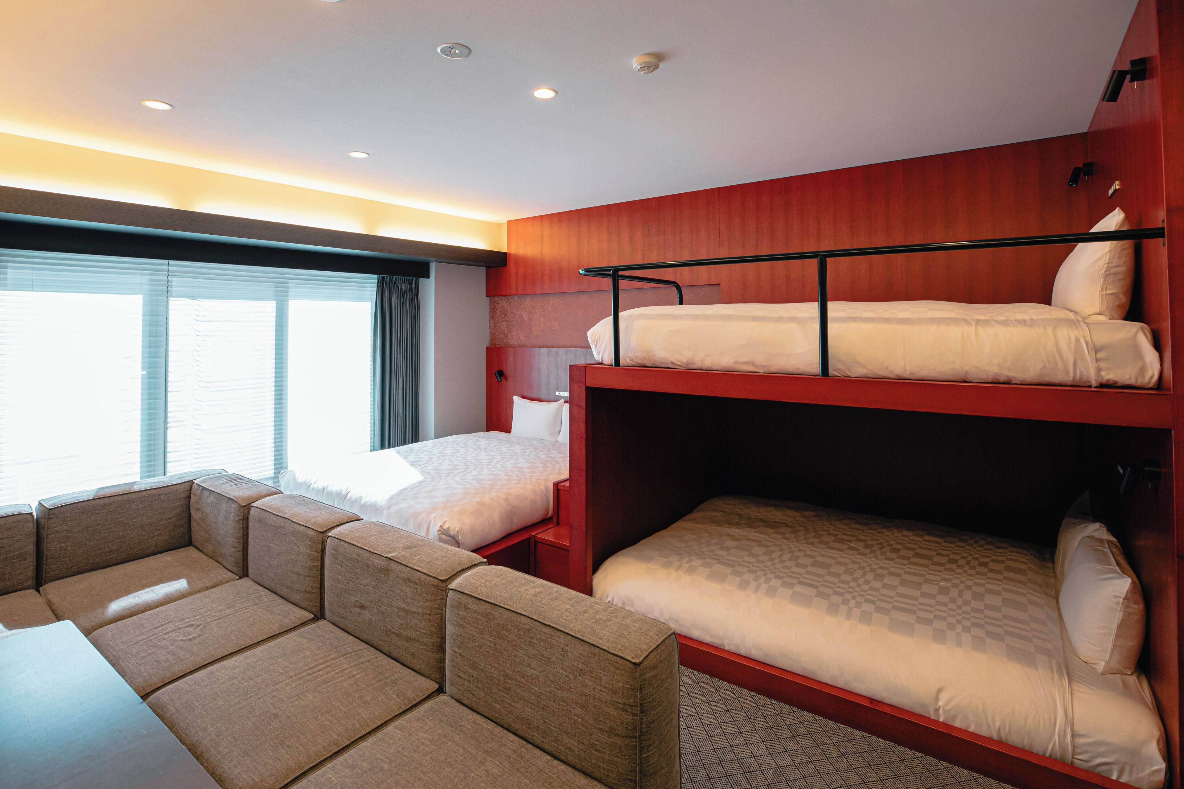 Ein Hotelzimmer mit zwei Einzelbetten, einer Schlafcouch und einem großen Fenster mit Vorhängen.