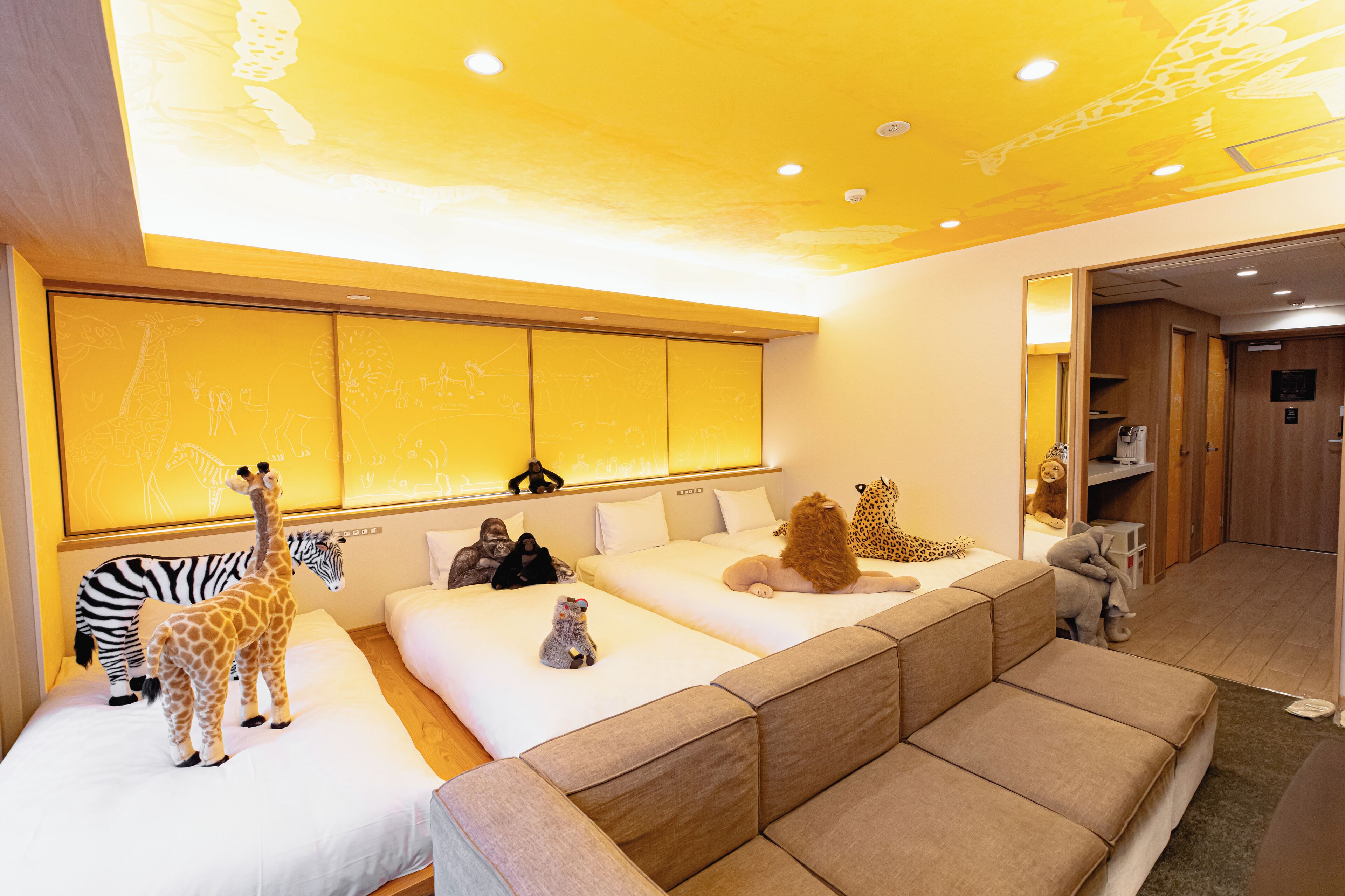 A hotel room with a large bed, a sofa, and a wall with animal drawings.