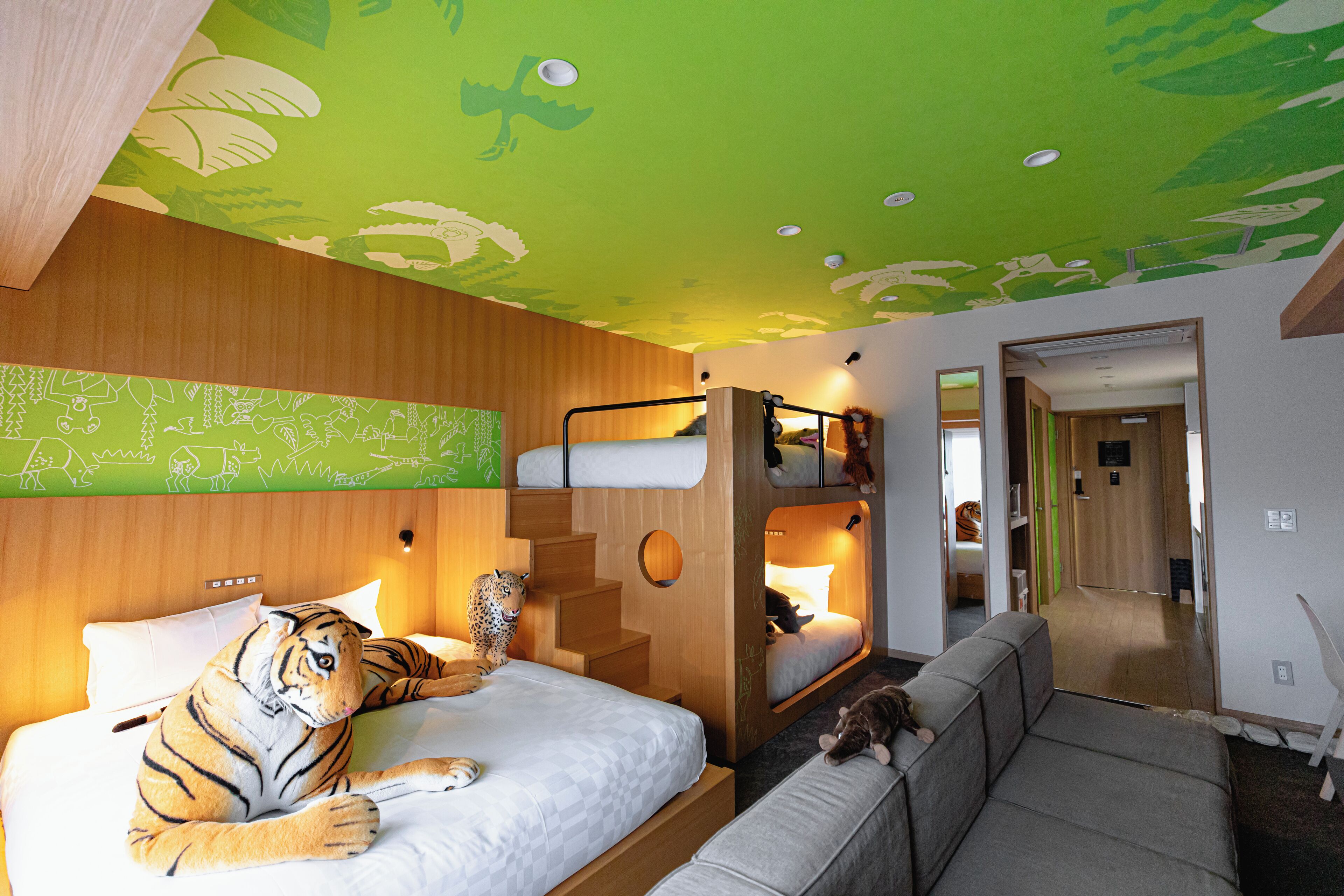 A room with a bed, a sofa, a cat, and a tiger plush toy.