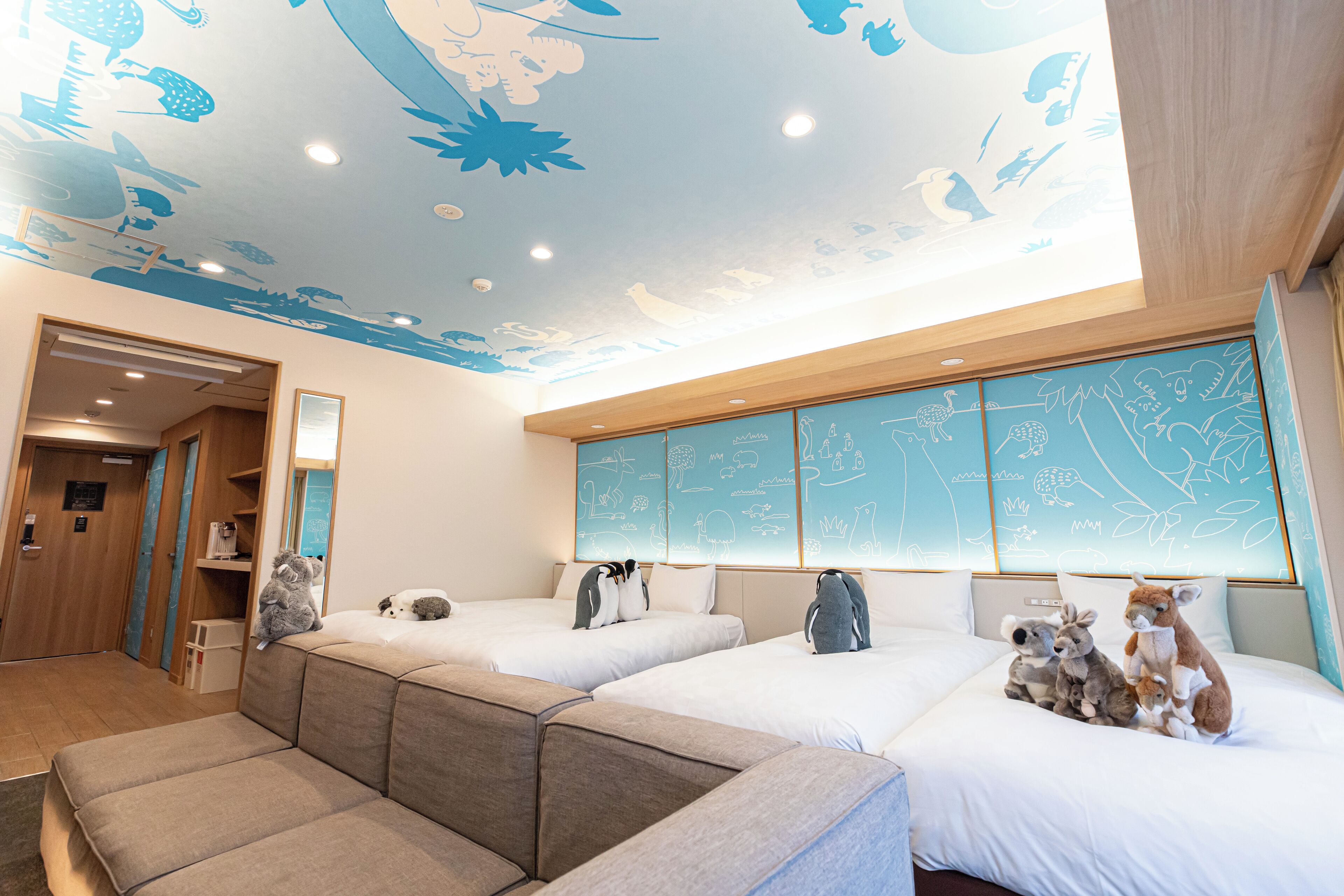 A hotel room with two beds, a sofa, and a ceiling with animal illustrations.