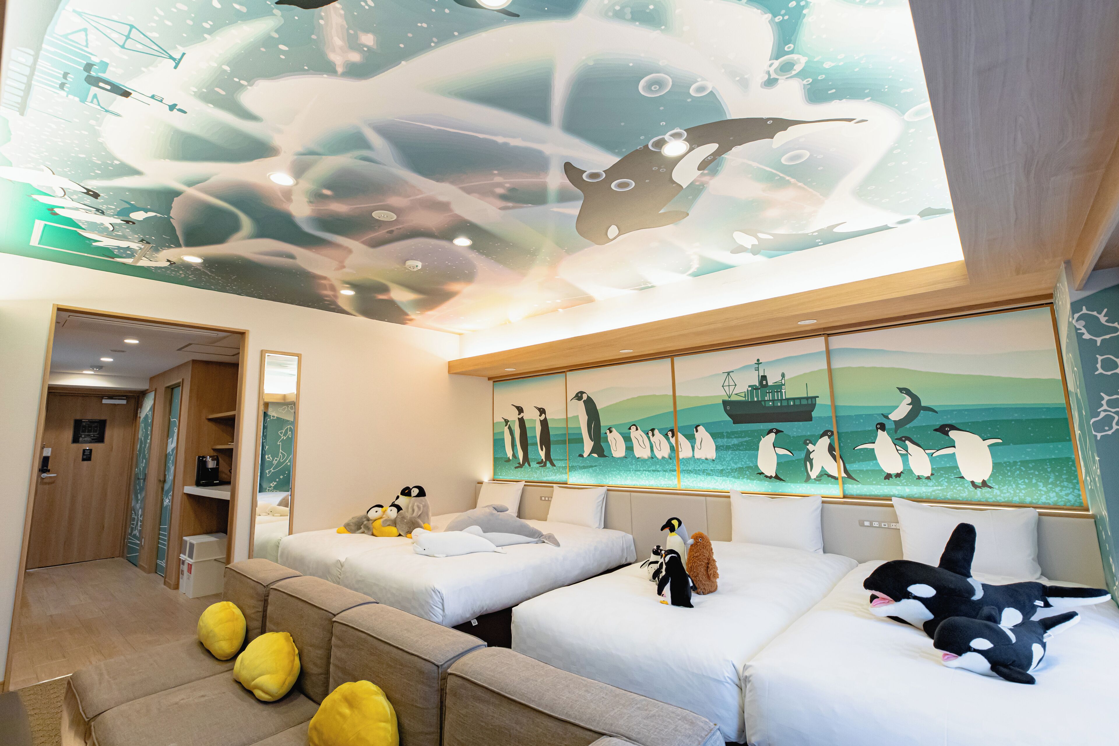 A hotel room with two beds, a sofa, and a ceiling mural of penguins and a ship.