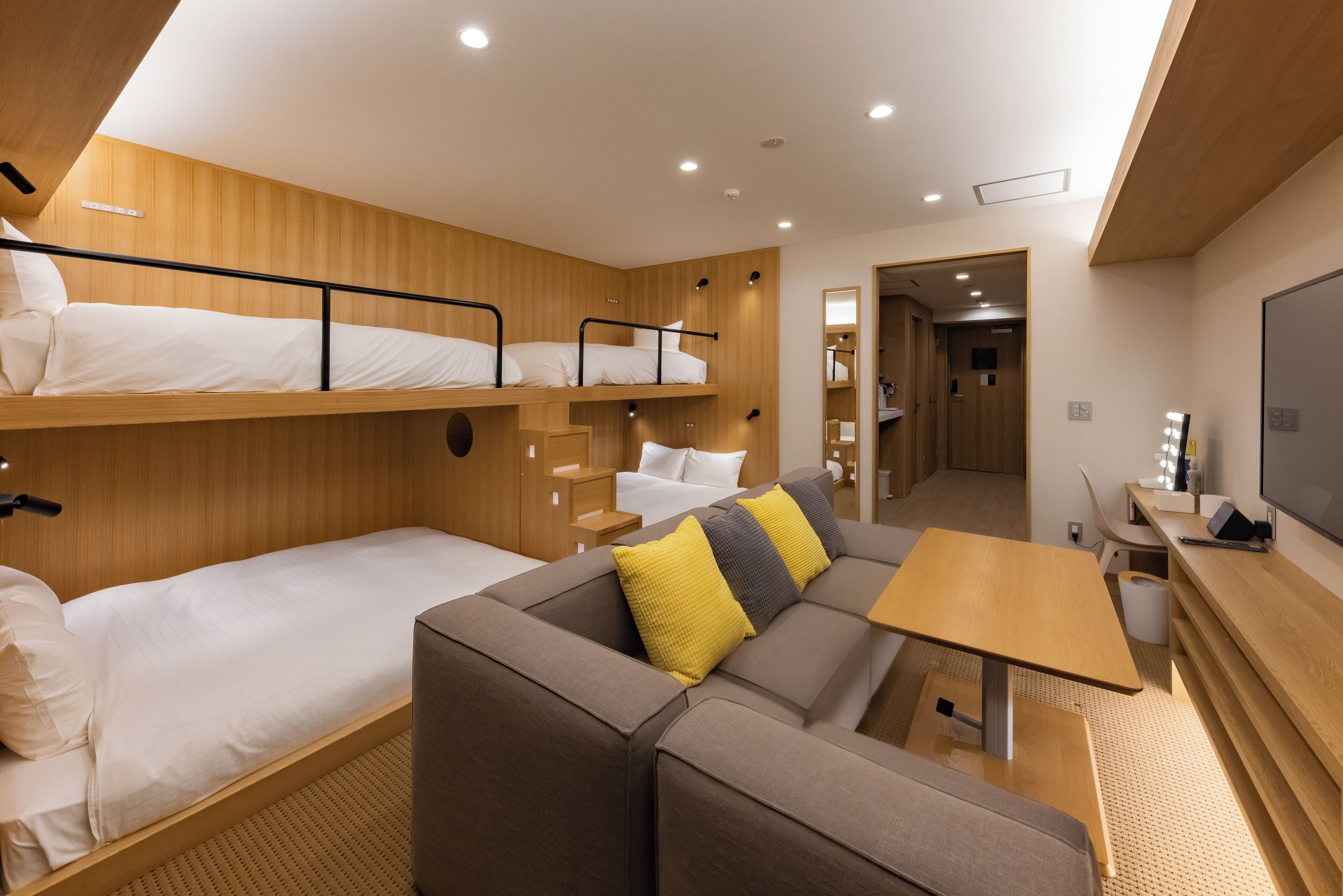 A modern hotel room with bunk beds, a sofa, a small table, and a TV.