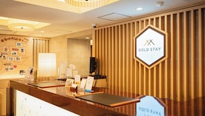 A reception desk with a wooden panel wall, a sign reading "GOLD STAY," and a map on the wall. - GOLDSTAY SAKAE (Nagoya)