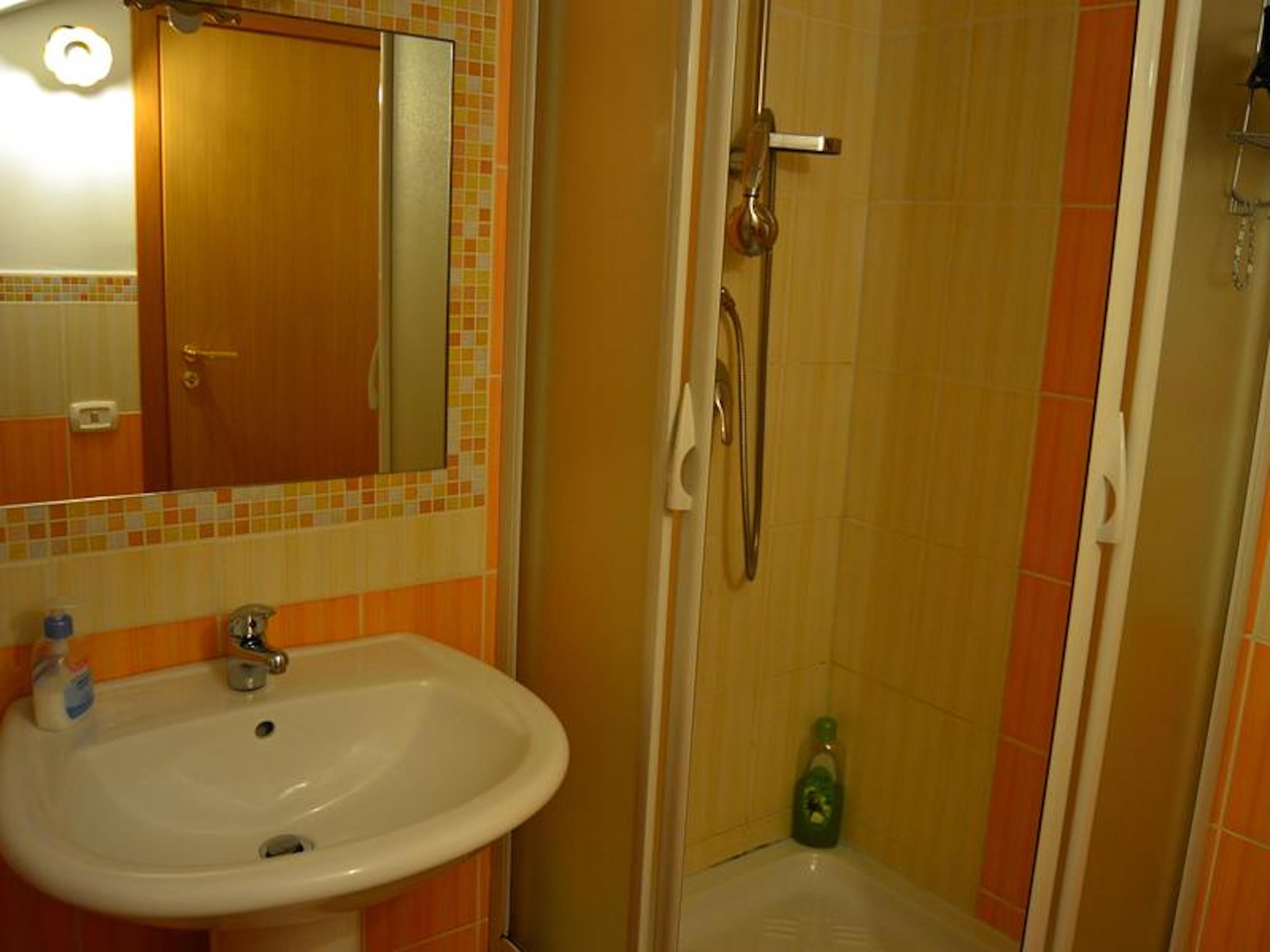 A bathroom with a sink, mirror, shower, and tiled walls.