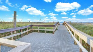 Een houten looppad naar een strand, met een heldere lucht.