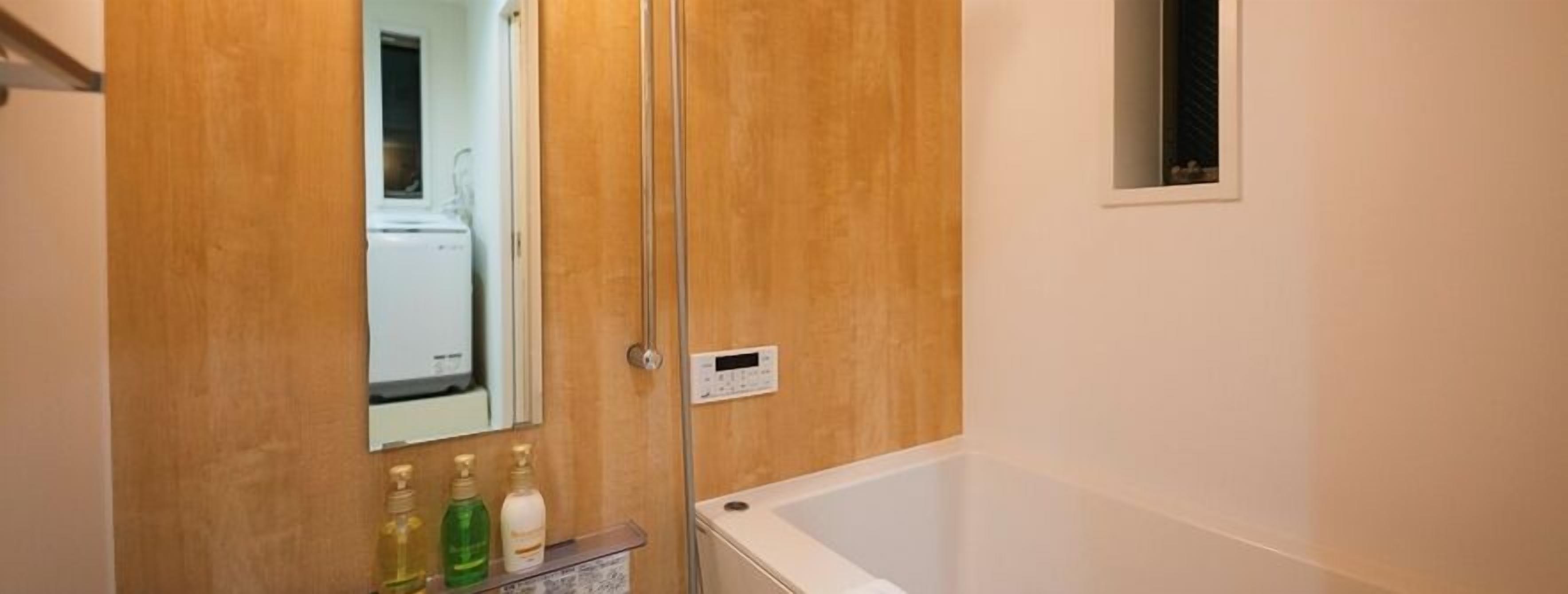A bathroom with a wooden door, a mirror, a control panel, and a bathtub.
