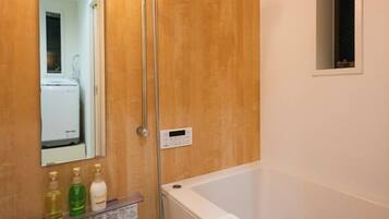 A bathroom with a wooden door, a mirror, a control panel, and a bathtub.