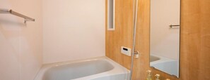 Een badkamer met een bad, een houten deur en een spiegel.