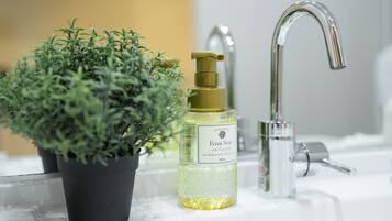 A bathroom sink with a glass bottle of foam soap and a potted plant.