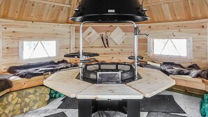 A wooden interior with a central black stove, wooden walls, and fur-lined benches.