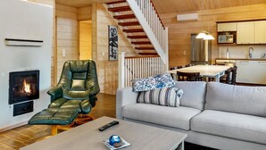 A cozy living room with a fireplace, a leather chair, a sofa, and a dining area with a staircase.