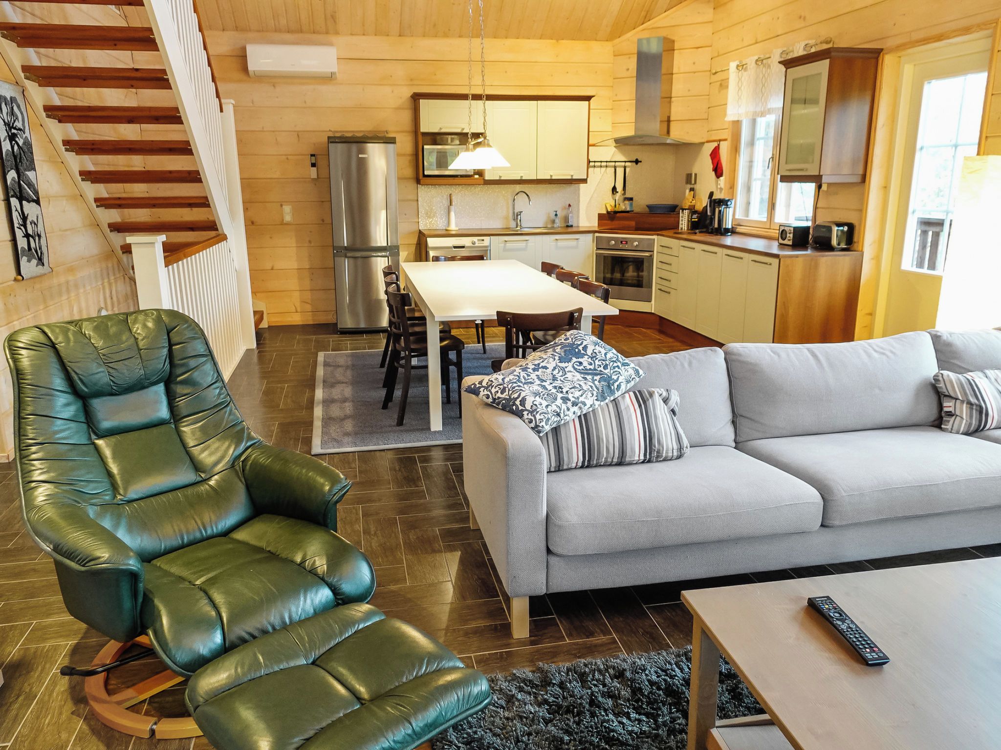 Ein modernes Wohnzimmer mit Ledersessel, grauem Sofa und Essbereich mit Tisch und Stühlen.