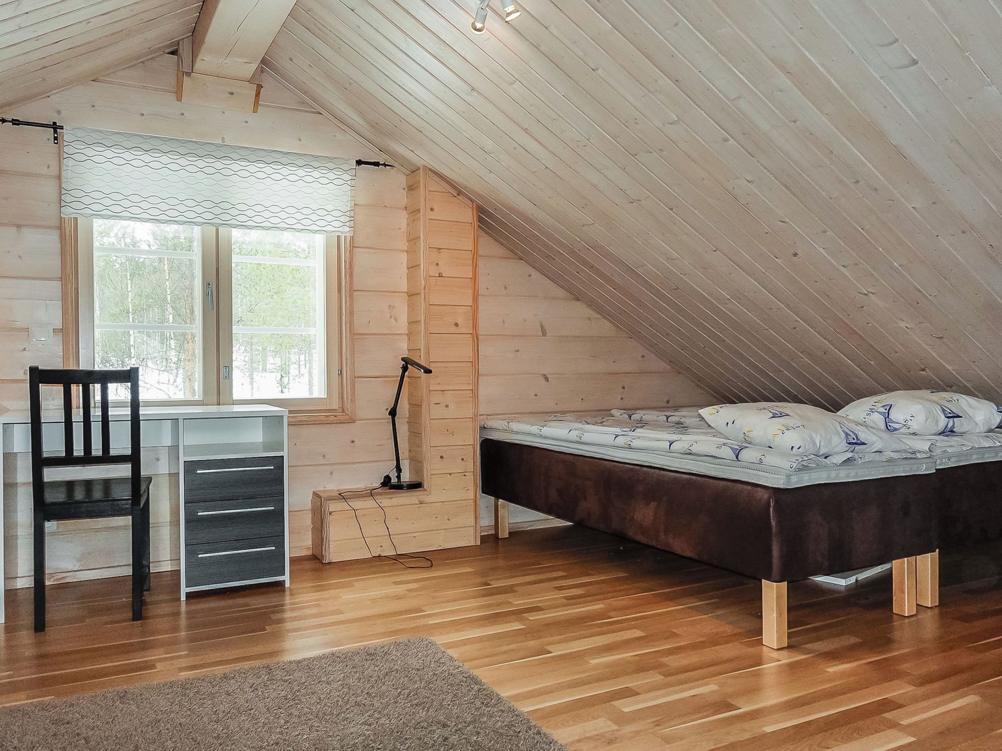 A bedroom with a sloped ceiling, a desk, a chair, a bed, and a window.