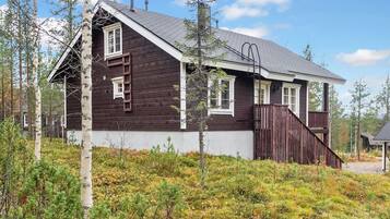 A wooden cabin with a sloped roof, a wooden porch, and a ladder leading to the upper windows.