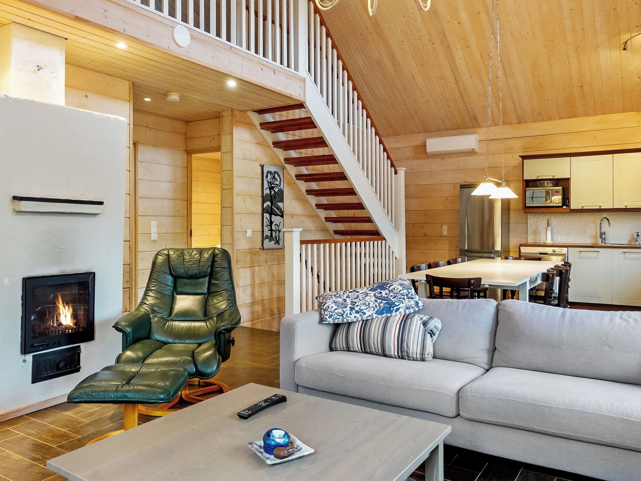 A cozy living room with a fireplace, a comfortable leather chair, a sofa with patterned cushions, a dining area with a table and chairs, and a kitchen with modern appliances.