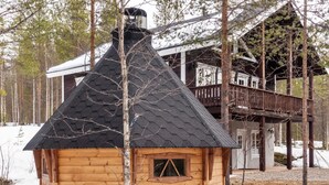 A wooden cabin with a steeply pitched roof, surrounded by trees and snow.