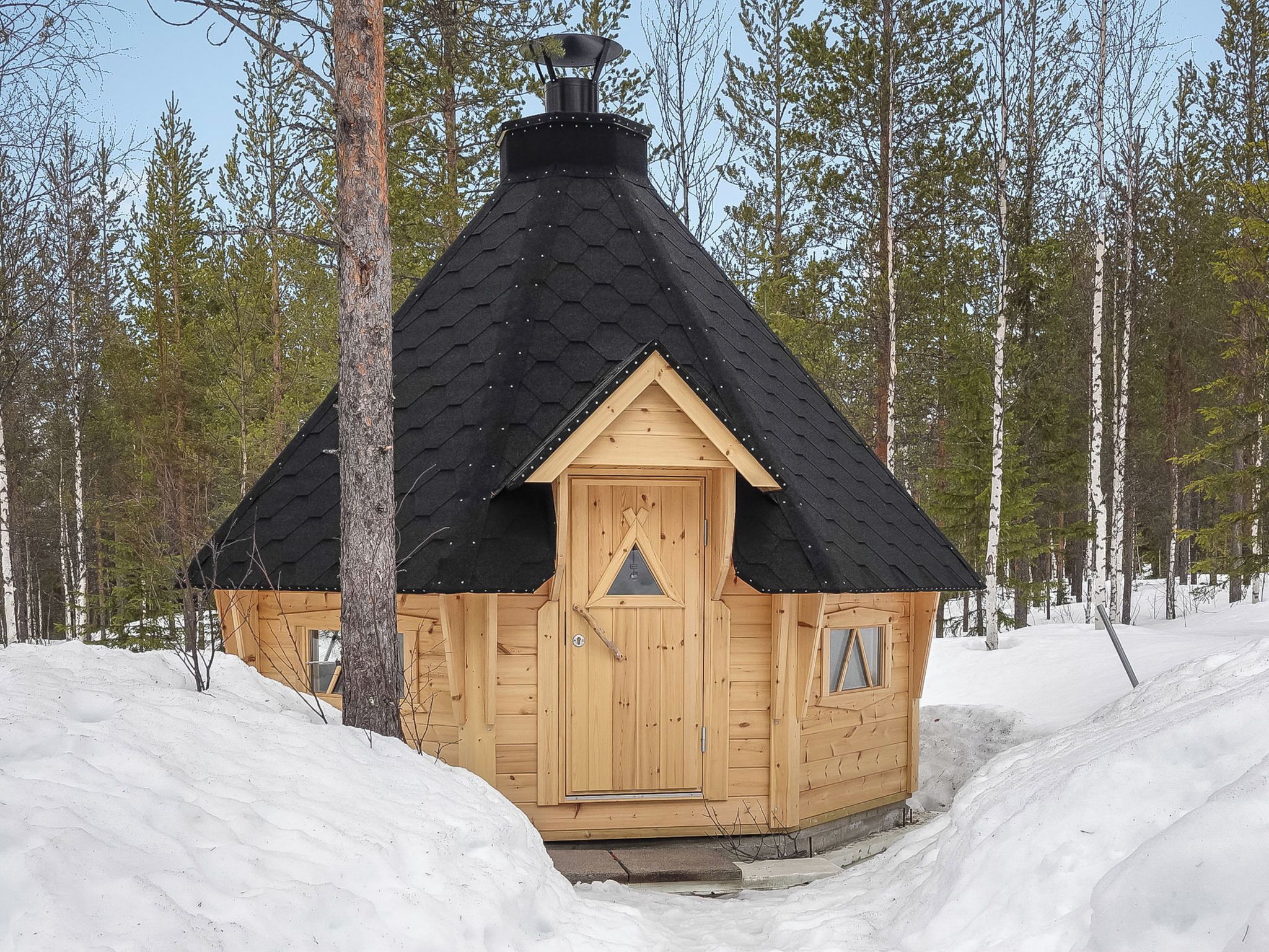 A wooden cabin with a black roof, surrounded by snow and trees.