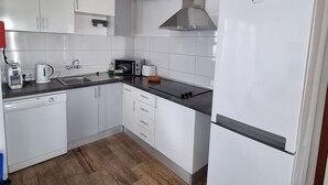 A modern kitchen with white cabinets, a stainless steel range hood, a built-in dishwasher, and a refrigerator.