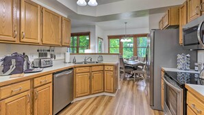 A kitchen with wooden cabinets, stainless steel appliances, a dishwasher, and a dining area with a table and chairs. - Blue Ridge Mtn Views: Condo w/ Furnished Balcony (Burnsville)