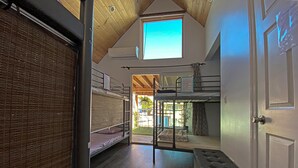 A dormitory room with bunk beds, a wooden ceiling, and a window.